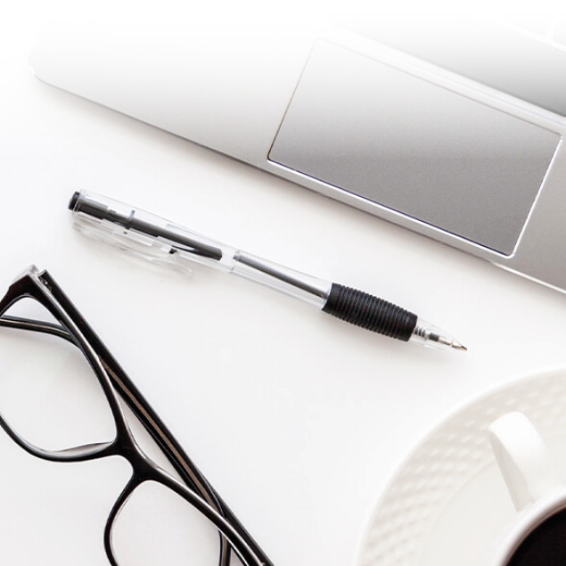 Laptop, Brille und Stift auf weissem Tisch